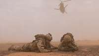 Zwei Soldaten der Bundeswehr liegen am Boden, während ein Hubschrauber abhebt