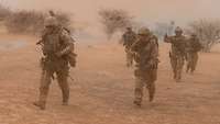 Mehrere Soldaten der Bundeswehr im Gelände gehen durch aufgewirbelten Staub 