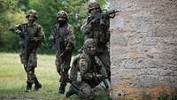 Vier Soldaten stehen hinter einer Hauswand in Deckung.