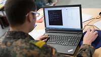 Ein Bundeswehrsoldat sitzt vor einem geöffneten Laptop