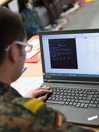 Ein Bundeswehrsoldat sitzt vor einem geöffneten Laptop