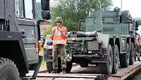 Ein Soldat steht auf einem Waggon und gibt einem LKW Fahrer Handzeichen.