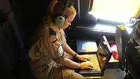 Eine Soldatin sitzt mit Kopfhörern vor einem Laptop 