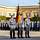 Three service men in basic dress, the one in the middle holds the flagpole with the Federal Institutions Flag