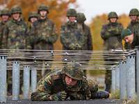 Mannschaften auf der Hindernisbahn Soldat kriecht unter einem Hindernis durch