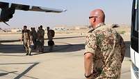 Ein Flugfeld mit mehreren Soldaten, rechts im Bild ein Teil eines Busses, links der Flügel eines Flugzeugs