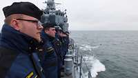 Marinesoldaten in blauer Arbeitsuniform stehen in Reihe auf dem Deck eines Kriegsschiffs.