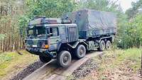 Ein Lastwagen in Flecktarn-Lackierung steht auf einem Hügel.