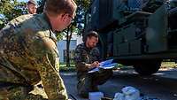 Ein Soldat kniet mit einem Ordner vor einem Lkw, zwei weitere Soldaten schauen zu.