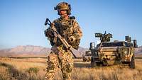 Ein Soldat steht vor einem Gefechtsfahrzeug, im Hintergrund hohe Berge