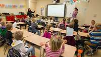 Kinder sitzen in einem Unterrichtsraum und schauen auf eine elektronische Tafel.