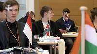Jugendliche sitzen an Tischen mit unterschiedlichen Länderflaggen