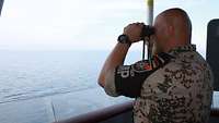 Ein Soldat schaut durch ein Fernglas auf das Meer 