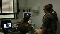 Ein Patientent wird von Ärzten mit Ultraschall untersucht, die Ärzte schauen auf einen Monitor mit den Ultraschallaufnahmen