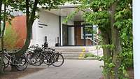 Ein Eingangsbereich mit Treppenaufgang zu einem Schulgebäude. Links stehen Fahrräder.