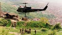 Ein Helikopter hebt eine Kiste in die Luft, Soldaten überwachen alles vom Boden