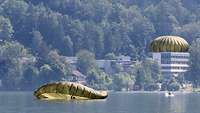 Zwei Fallschirmspringer tauchen in einen See ein. Im Hintergrund sind bewaldete Hänge.