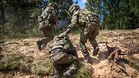 Drei Soldaten velassen einen Schützengraben zum Angriff. Einer stürmt voraus, der zweite hilft dem dritten aus dem Graben. 