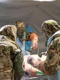 Drei Soldaten in persönlicher Schutzausrüstung duschen einen liegenden Patienten ab.