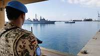 Ein Soldat der Bundeswehr am Ufer schaut auf ein Schiff, das in den Hafen einläuft.