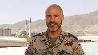 Hauptmann S. steht erhöht am Flughafen in Kabul vor einer Moschee. 