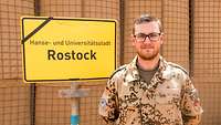 Ein deutscher Soldat steht vor dem Ortsschild Rostock im Camp Castor