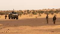 Drei deutsche Soldaten und ein Fahrzeug Typ Dingo stehen in der Wüste.