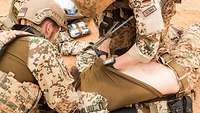 Soldaten tasten einen verletzten Soldaten nach Verletzungen ab.