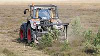 Ein Traktor mit Mulcher fährt über eine Grünfläche auf einem Truppenübungsplatz.