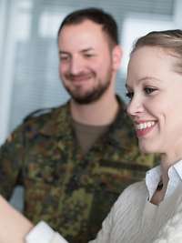 Frau und Soldat stehen vor Flipchart