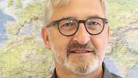 Terminologie im Bundessprachenamt - Was ist das? Portrait von Gerd Preißler vor einer Weltkarte.