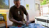 Ein Soldat verzurrt mit Metallbändern einen grauen Kunststoffcontainer, im Hintergrund der Container des Feldpostamts