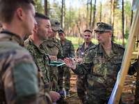 Kommandeur der eFP Battle Group bei der Befehlsausgabe Soldaten stehen im Wald und unterhalten sich