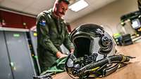 Ein Pilot, der seine Dienstkleidung prüft. Im Vordergrund ist sein Helm zu sehen.