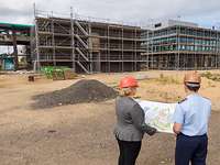 Eine Frau und ein Mann in Uniform schauen gemeinsam auf eine große Karte, im Hintergrund eine Baustelle.