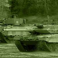 Ein Kampfpanzer fährt auf einer Freifläche neben einem Schützenpanzer.