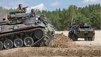Ein Pionierpanzer schiebt mit seinem vorn angebrachten Räumschild Erdmasse vor sich her.