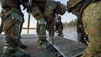 Vier Soldaten bringen bei Eis und Schnee an einer Metallbrücke eine Rampe an.