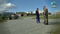 Ein Mann in Arbeitskleidung und zwei Soldaten in Flecktarn-Uniform stehen auf einem Übungsgelände der Bundeswehr.
