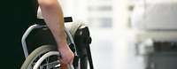 Eine männliche Person fährt im Rollstuhl den Flur einer Klink entlang