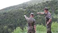 Zwei Soldaten stehen nebeneinander und deuten mit den Händen auf das Gelände im Hintergrund