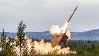 Ein Raketenwerfer schießt im Wald ein Rakete ab. Feuer und Rauch entstehen.