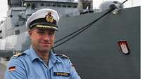 Ein Marineoffizier in blauer Uniform vor einem grauen Schiff