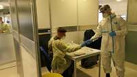 Ein Soldat in Schutzkleidung übergibt eine Probe an einen zweiten 