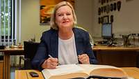Dr. Eva Högl sitzt an einem Schreibtisch und trägt sich ins Gästebuch ein