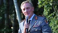 Ein Soldat im grauen Dienstanzug hat im Freien ein Mikrofon in der Hand.