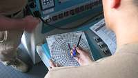 Ein Soldat hält einen Stift und ein Navigationsblatt in der Hand, dass wie ein Spinnennetz aussieht