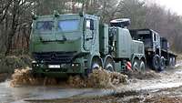 Das Berge- und Abschleppfahrzeug Bison fährt durch eine Wasserlache mit einem LKW am Haken.